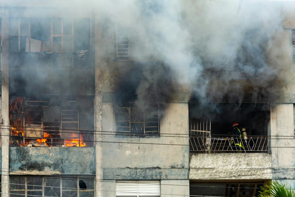 A firefighter battling flames and smoke on a residential building's balcony during a fire incident.